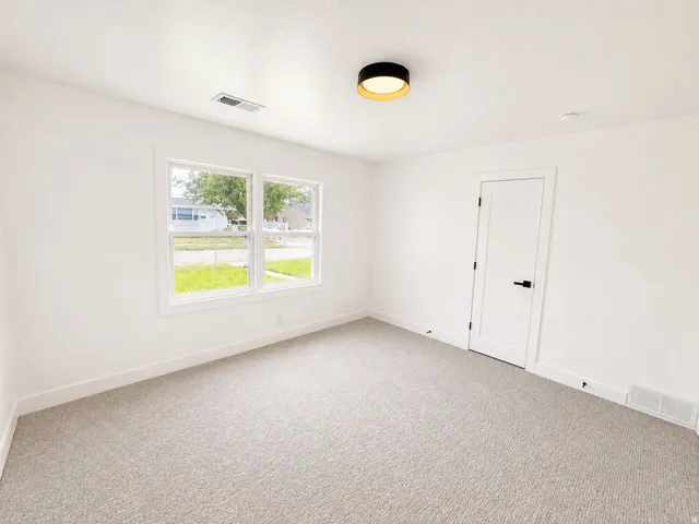 White interior walls, light-colored carpet flooring, a contemporary ceiling light fixture, white interior door with black hardware, and two windows