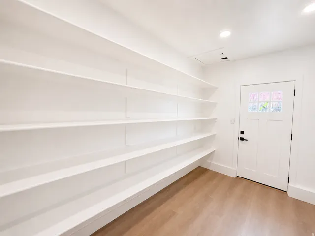 Extensive built-in shelving, wood-finish flooring, recessed lighting, and a white paneled door with black hardware
