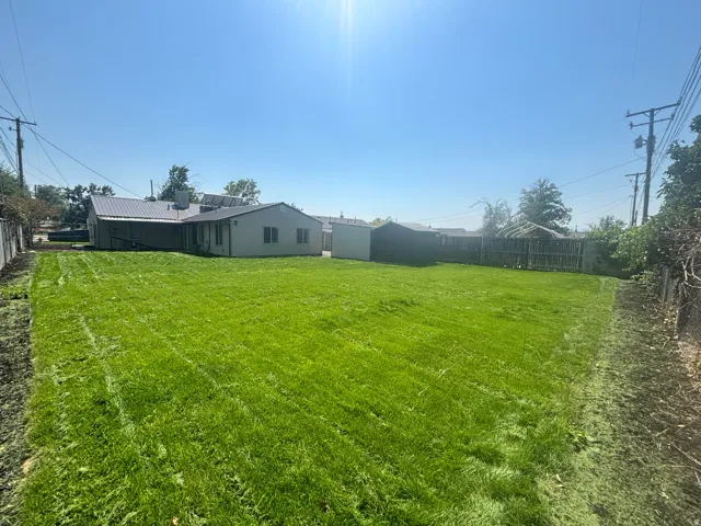 Expansive lawn with a metal roof on the primary structure, a covered patio, and a privacy fence