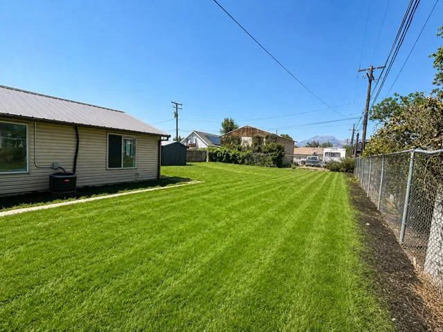 Expansive backyard featuring a manicured lawn, a metal storage shed, and a chain-link fence