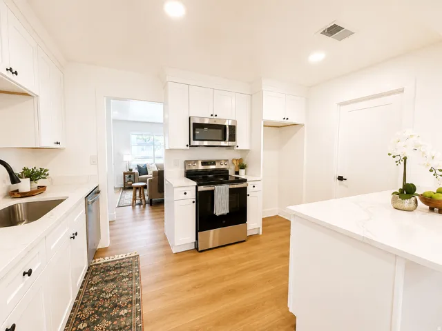 Kitchen featuring white cabinetry, stainless steel appliances, light-toned countertops, and wood-finish flooring