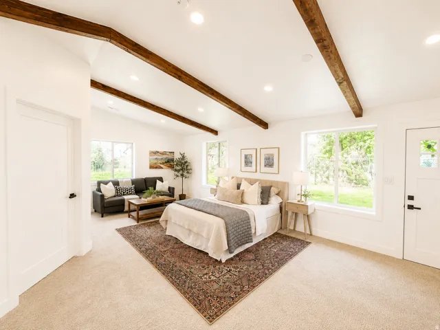Vaulted white ceilings with exposed wood beams, large windows, recessed lighting, and neutral carpeting