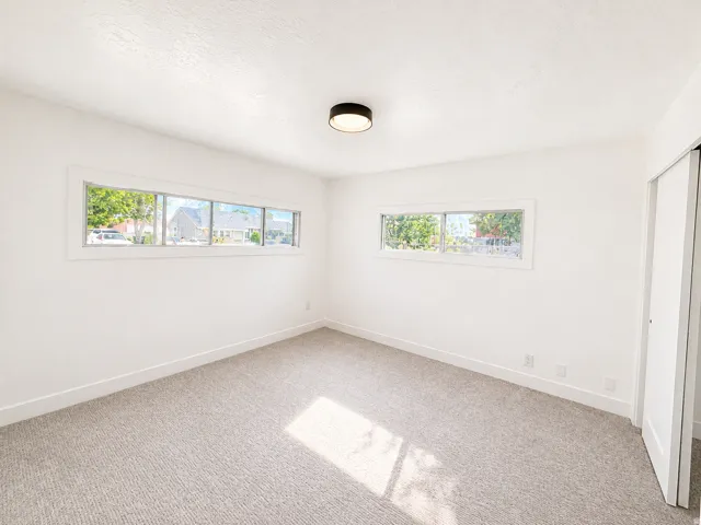 White walls with neutral carpet flooring, featuring a flush-mount ceiling light fixture, multiple horizontal windows, and a white interior door