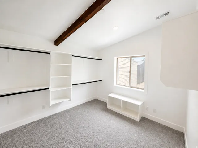 Vaulted ceiling with exposed wood beam, recessed lighting, built-in shelving, carpet flooring, and a window for natural light