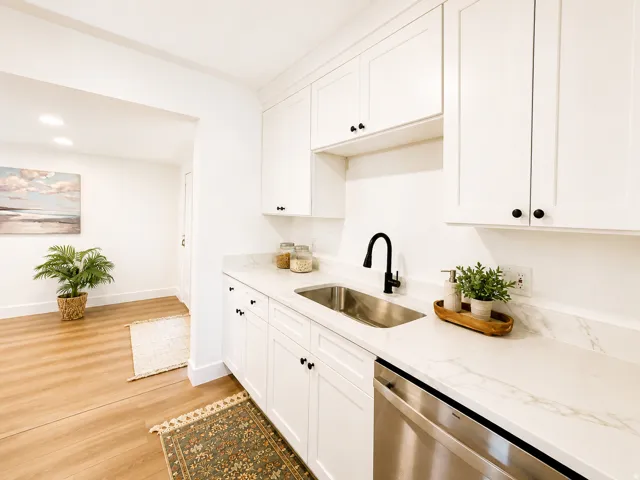 White shaker cabinetry, stainless steel dishwasher, undermount sink with a matte black gooseneck faucet, light-toned wood-finish flooring, and white countertops with subtle veining
