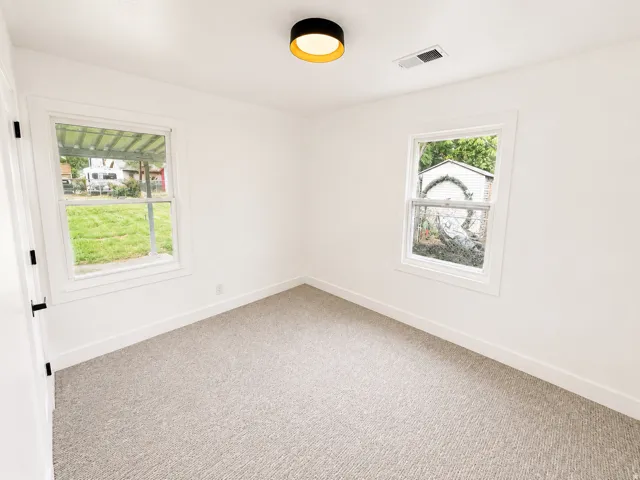Plush gray carpeting, white painted walls, and two double-hung windows