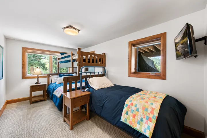 Wall-mounted television, wood-trimmed windows, built-in bunk beds, light-toned carpet, and a flush-mount ceiling light fixture
