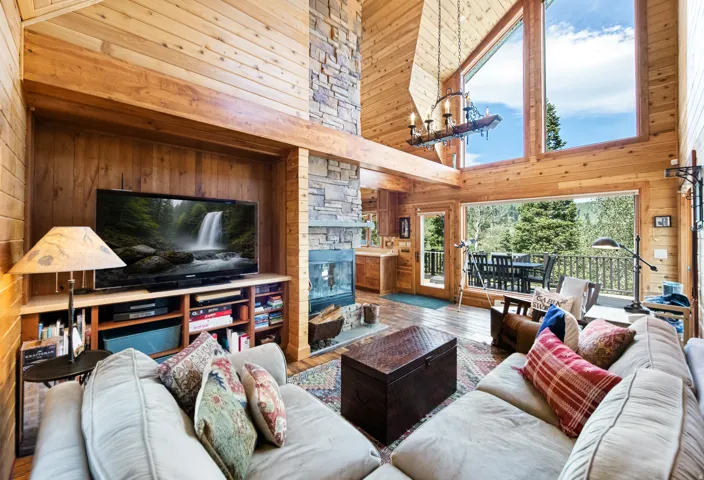 Vaulted wood-paneled ceilings, stone-clad fireplace, built-in media center, floor-to-ceiling windows, and a private balcony