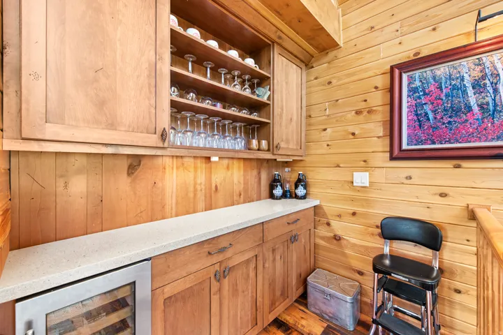 Wood-paneled walls and ceiling, wood-finish flooring, built-in wooden cabinetry, light-toned countertop, and an integrated beverage cooler