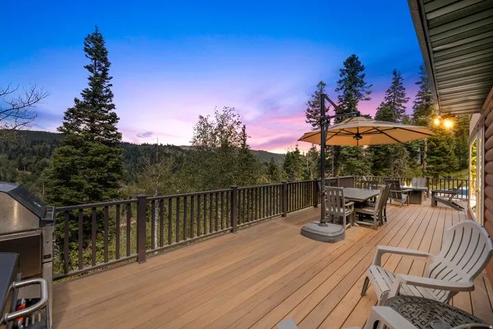 Expansive outdoor deck with wood-finish flooring, dark wood railing, and surrounding evergreen trees