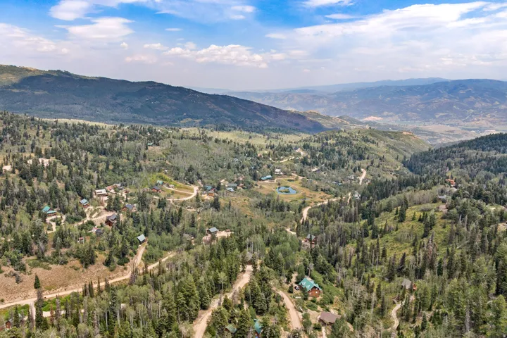 Expansive mountainous terrain with varied tree coverage, multiple residential structures, and winding unpaved roads