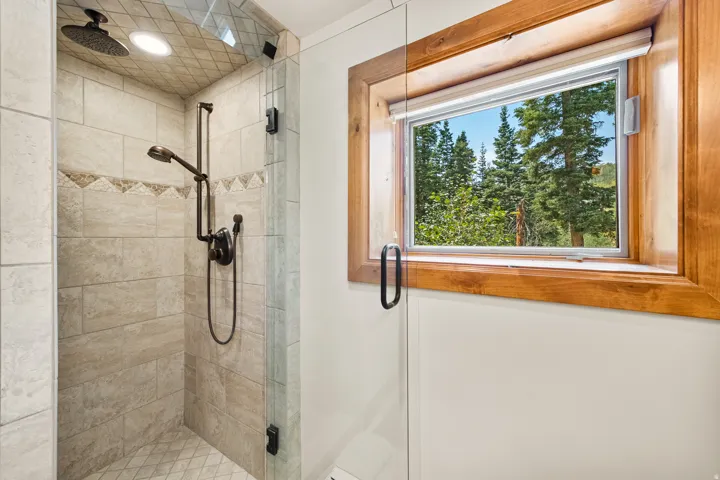 Tiled shower enclosure with a rain shower head, hand-held shower fixture, and glass shower door