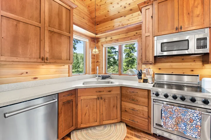 Wood-paneled kitchen featuring stainless steel appliances, wood cabinetry, light-toned countertops, and a stainless steel sink