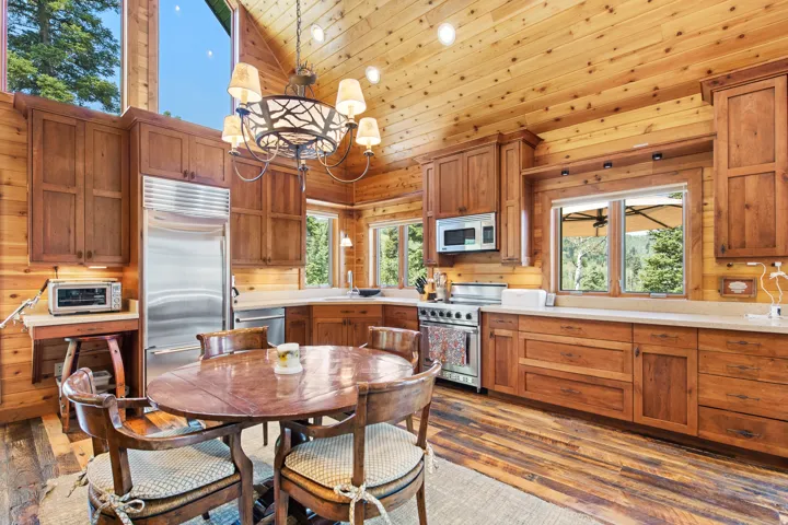 Wood-paneled vaulted ceiling, natural wood-finish flooring, stainless steel appliances, wood cabinetry, and a large picture window