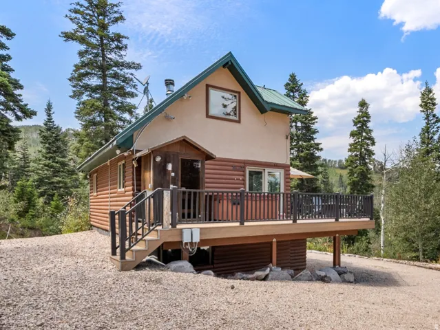 Wood-sided dwelling with a green pitched roof, featuring a raised deck with dark railings