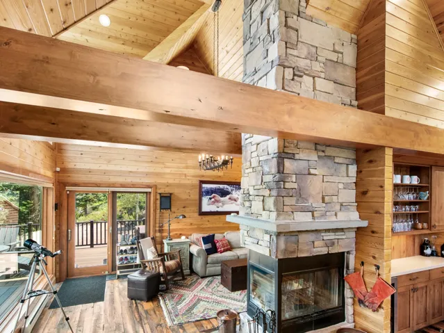 Vaulted wood-paneled ceilings with exposed wood beams, a stone fireplace, wood-finish flooring, and built-in cabinetry