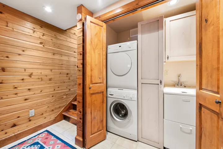 Laundry area featuring stacked appliances, a utility sink, and wood-finish cabinetry