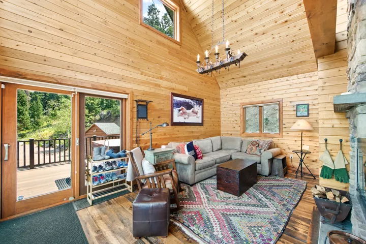 Vaulted wood-paneled ceilings, wood-finish flooring, stone-clad fireplace with mantel, and sliding glass doors to outdoor deck