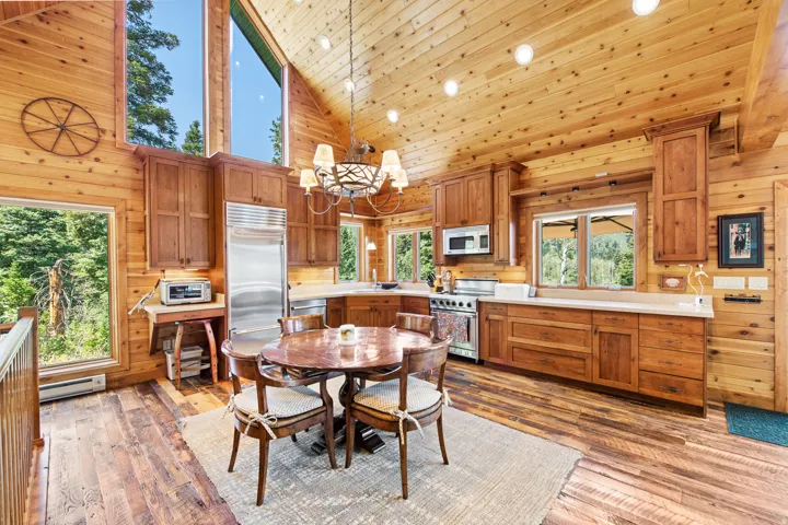 Vaulted wood-paneled ceiling, wood-finish flooring, custom wood cabinetry, stainless steel appliances, and large picture windows