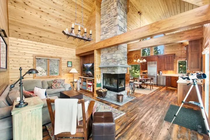 Vaulted wood-paneled ceilings, a stone-clad fireplace, wood-finish flooring, exposed wood beams, and a well-appointed kitchen with stainless steel appliances