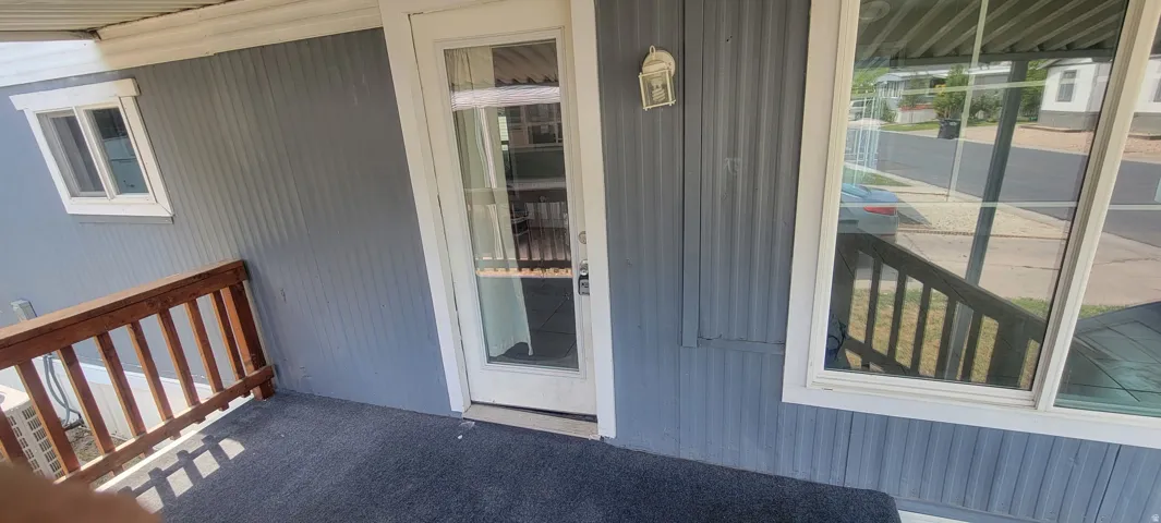 Corrugated siding with a full-light storm door, white window trim, and a porch light fixture