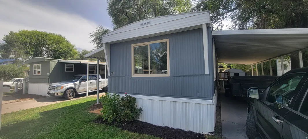 Exterior featuring a light blue facade, white trim, a single-pane window, and a covered carport with a metal roof