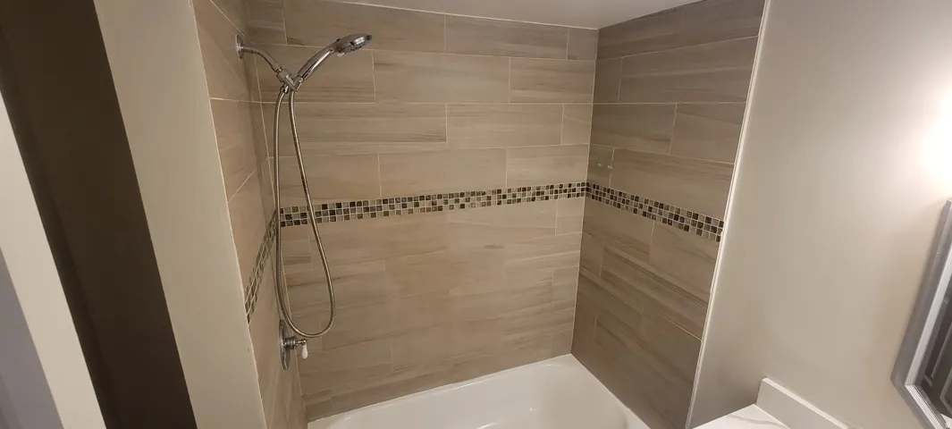 Bathtub with a tiled surround featuring a decorative mosaic accent band