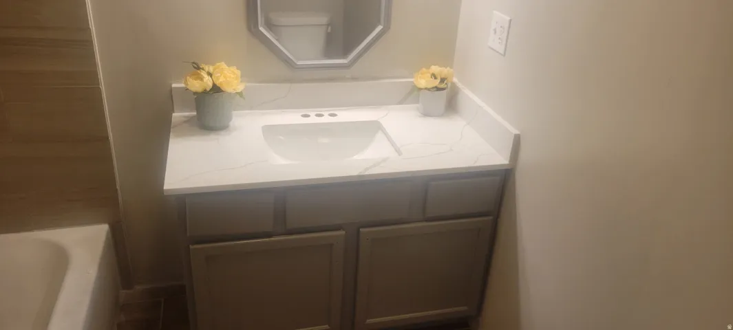 Vanity featuring a white countertop with integrated sink, gray cabinetry, and a framed octagonal mirror