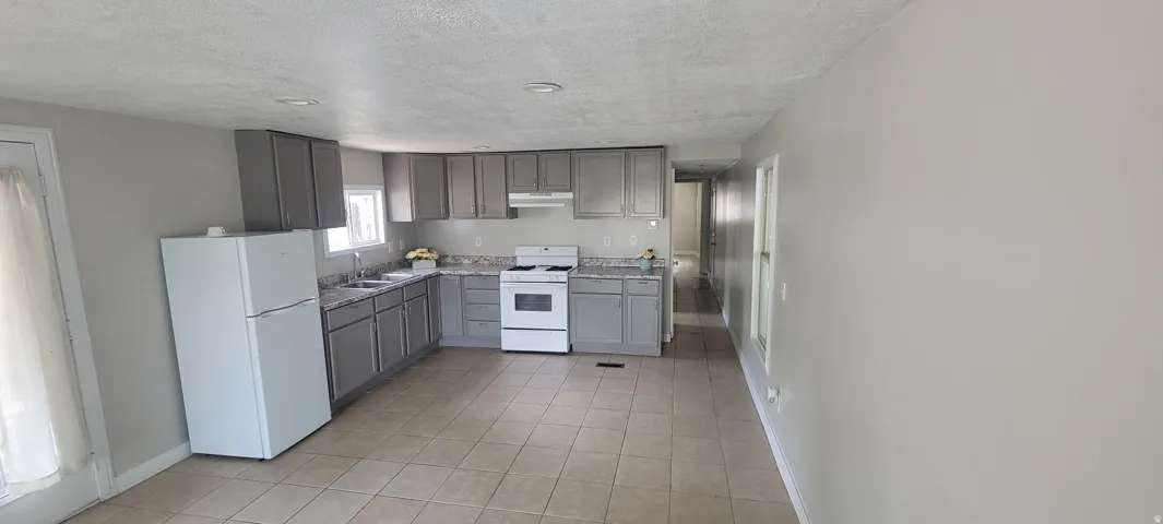 Kitchen featuring gray cabinetry, light-toned tiled flooring, white appliances, and recessed lighting
