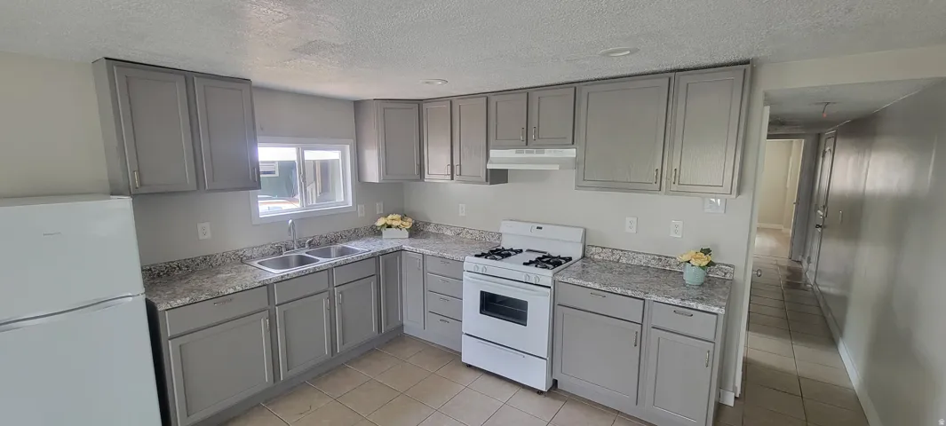 Kitchen featuring gray cabinetry, white appliances, dual basin sink, and tiled flooring