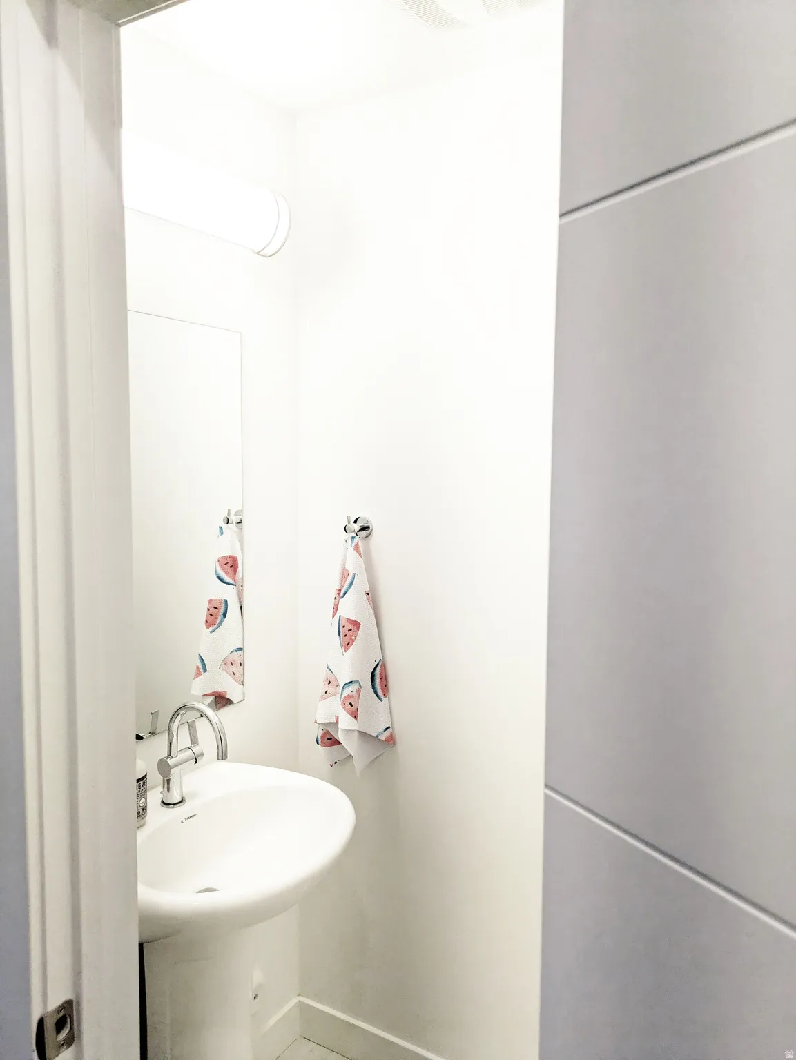 Pedestal sink with a chrome faucet, wall-mounted mirror, and overhead lighting