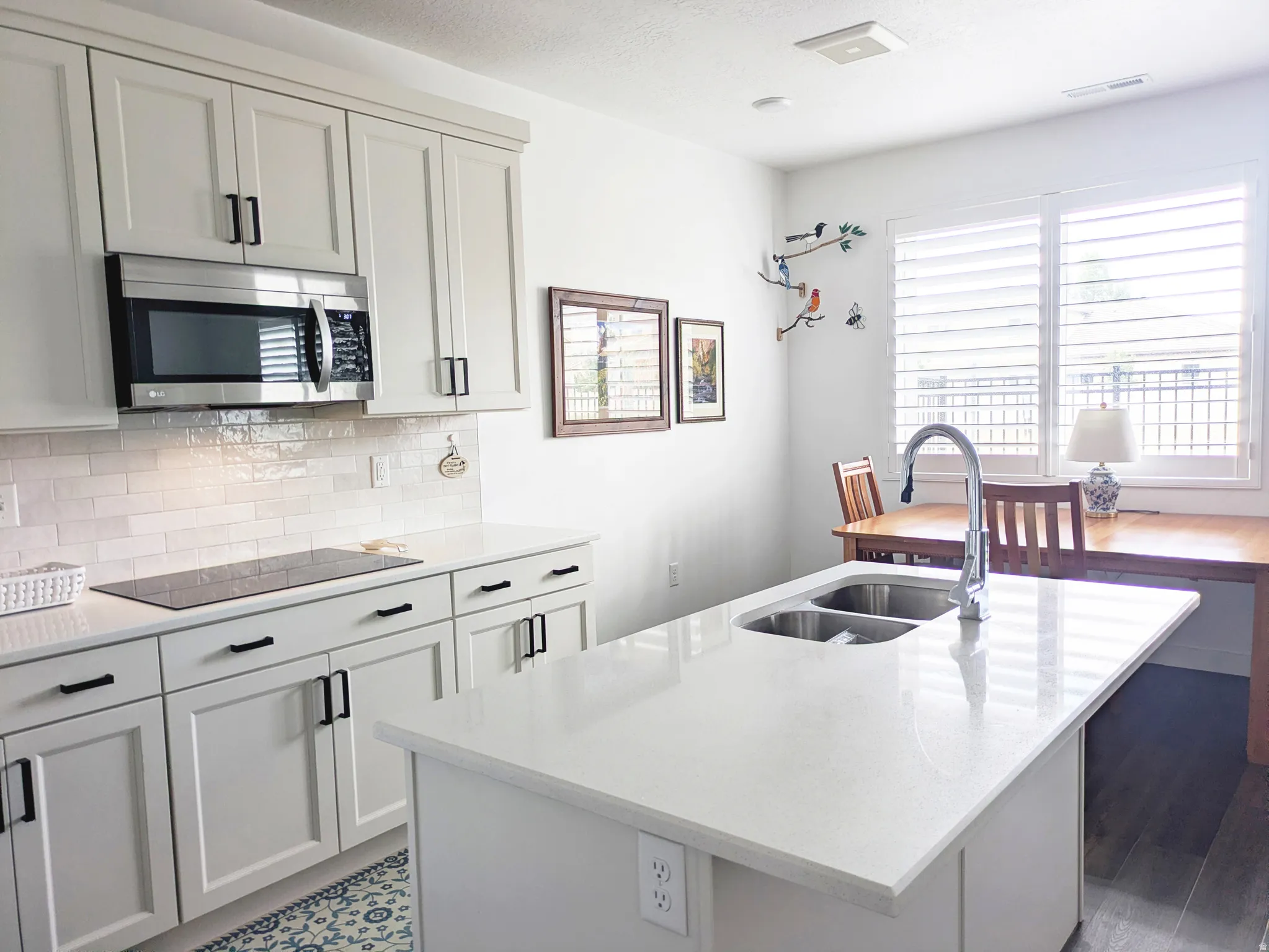 Kitchen featuring white shaker cabinetry, stainless steel microwave, white subway tile backsplash, and light-colored countertops