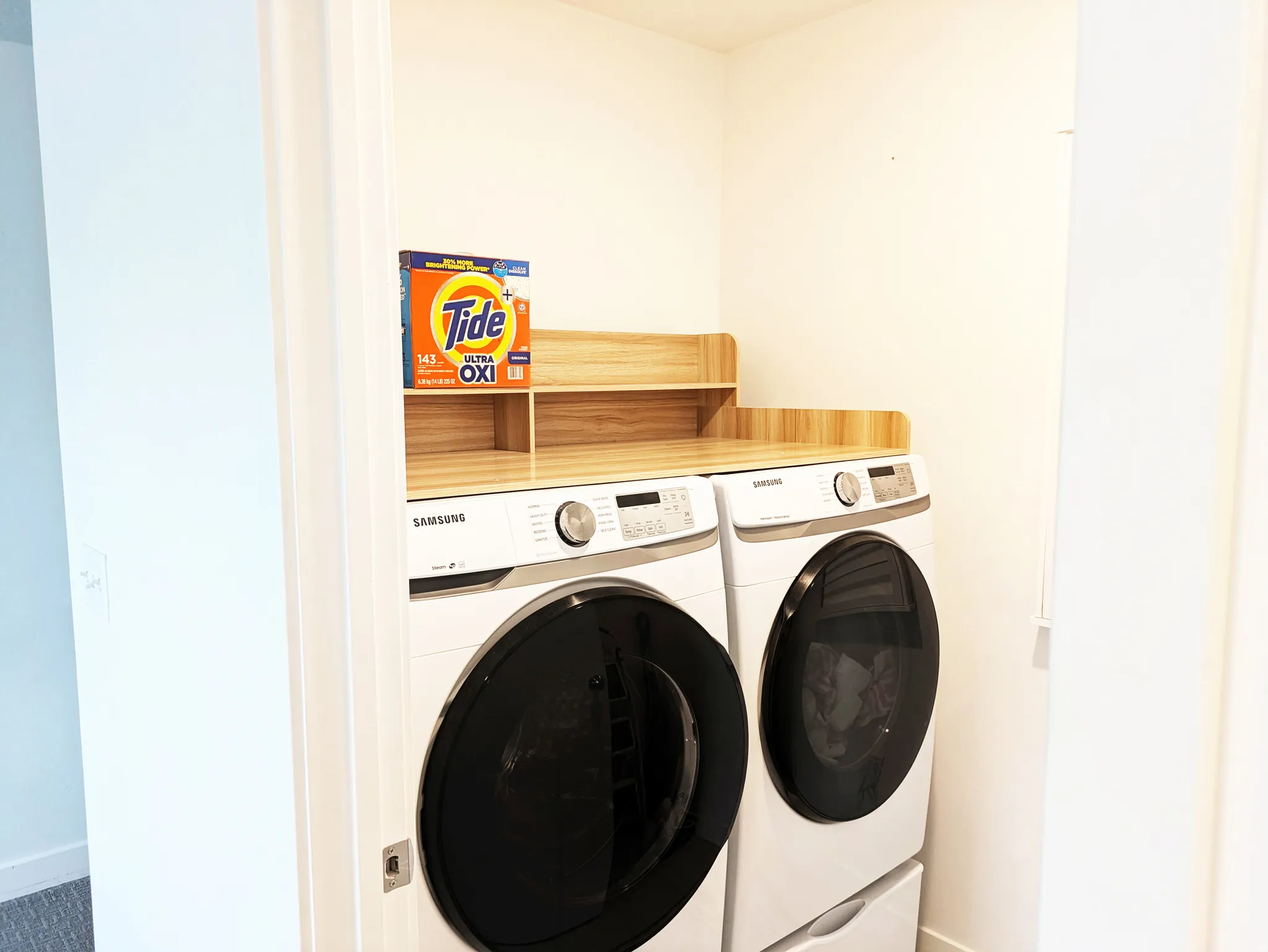 Dedicated laundry area featuring a front-loading washer and dryer, wood-finish countertop, and integrated shelving