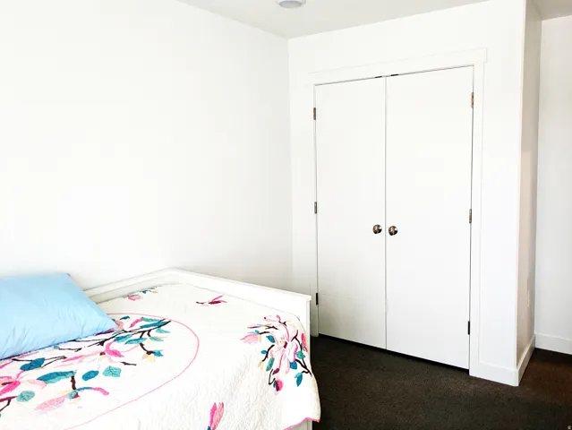 White walls, bi-fold closet doors with round hardware, and dark carpet flooring