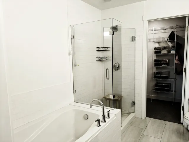 Shower with clear glass enclosure, white subway tile surround, and built-in shelving