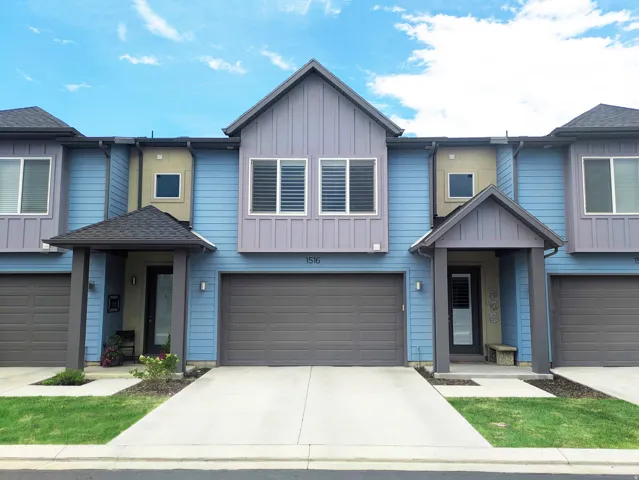 Multi-level residential facade featuring vertical and horizontal siding, attached two-car garage, covered entry, and individual driveways