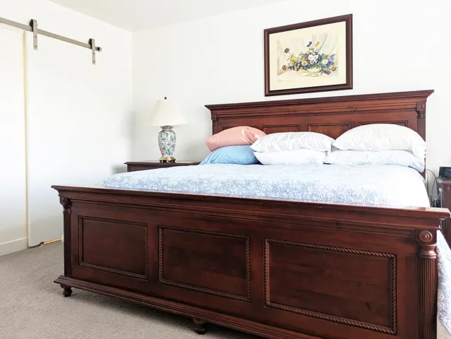 Hardwood bed frame with carved detailing, neutral carpeting, and a barn door hardware system