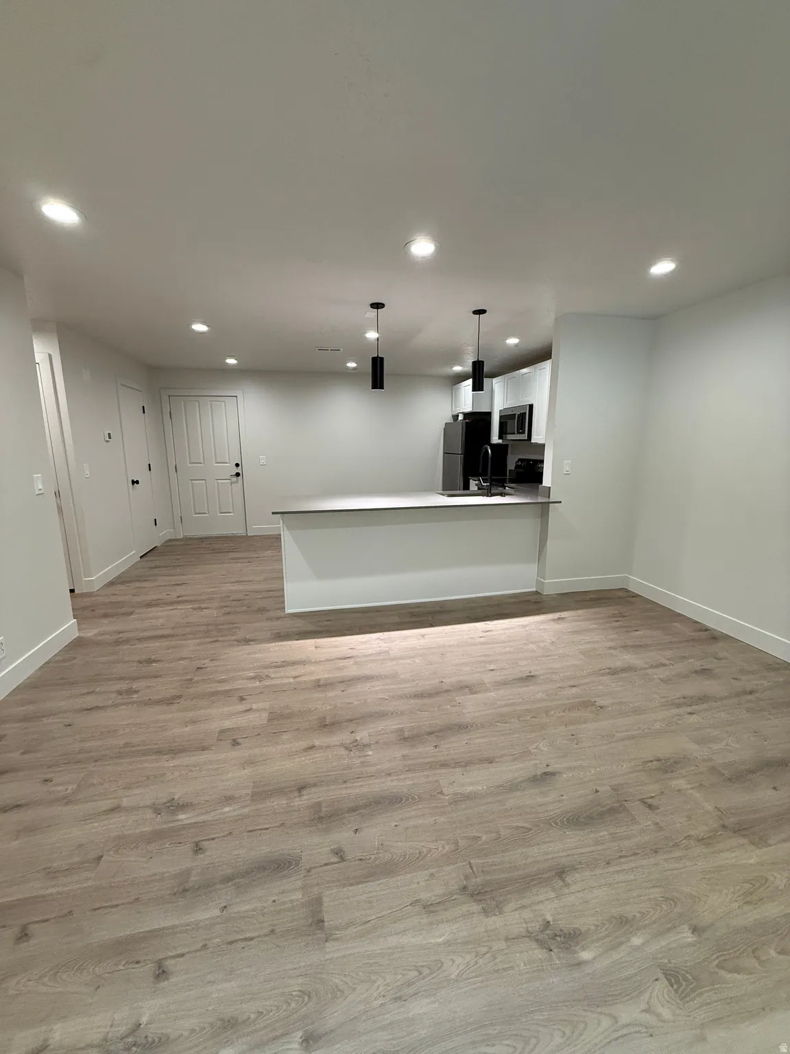 Open-concept living space with wood-finish flooring, recessed lighting, and a kitchen island with pendant lighting
