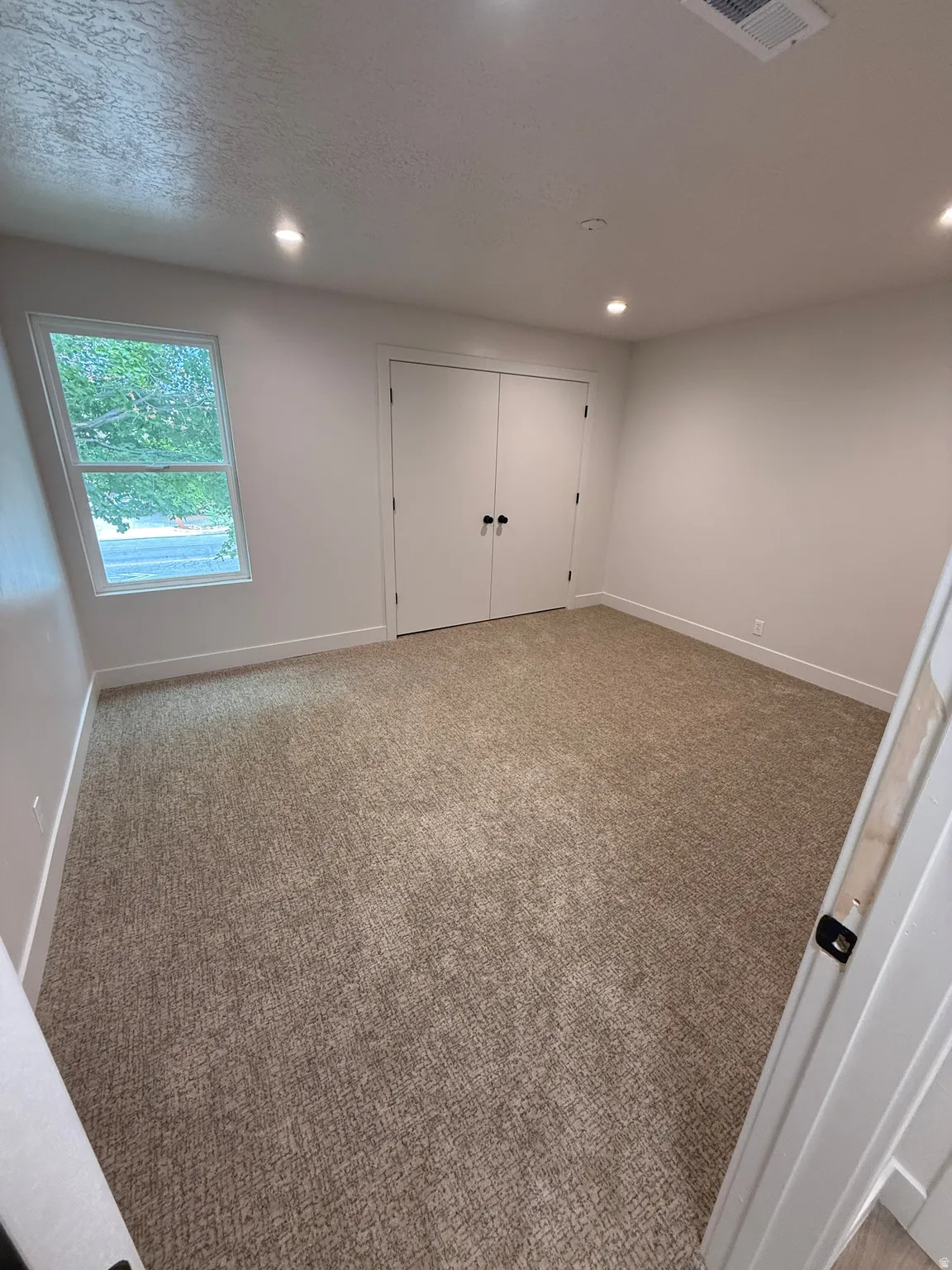 Recessed lighting, neutral-toned carpeting, white walls, and a double-door closet