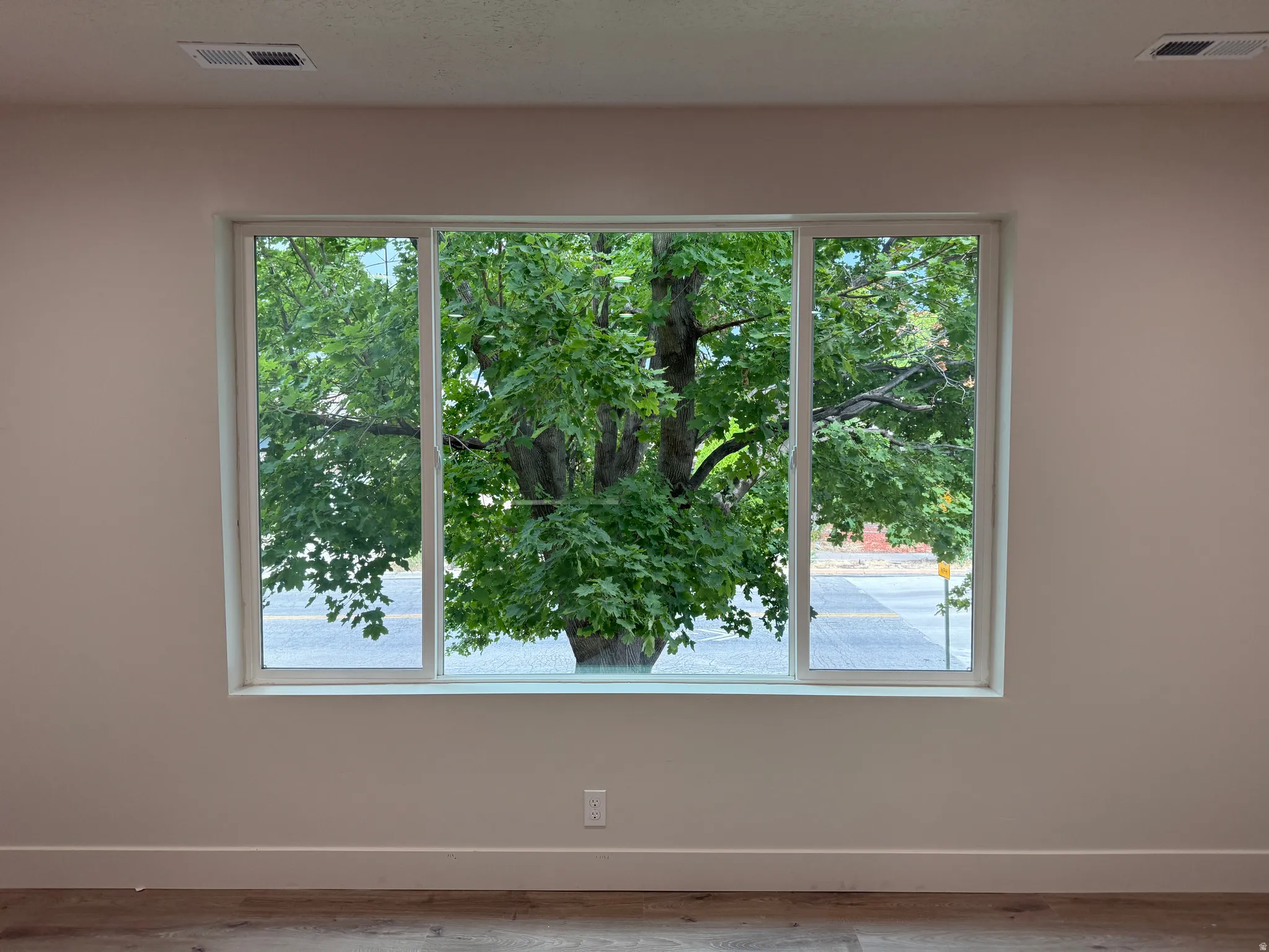 Expansive triple-pane window with white framing, light neutral wall paint, and wood-finish flooring