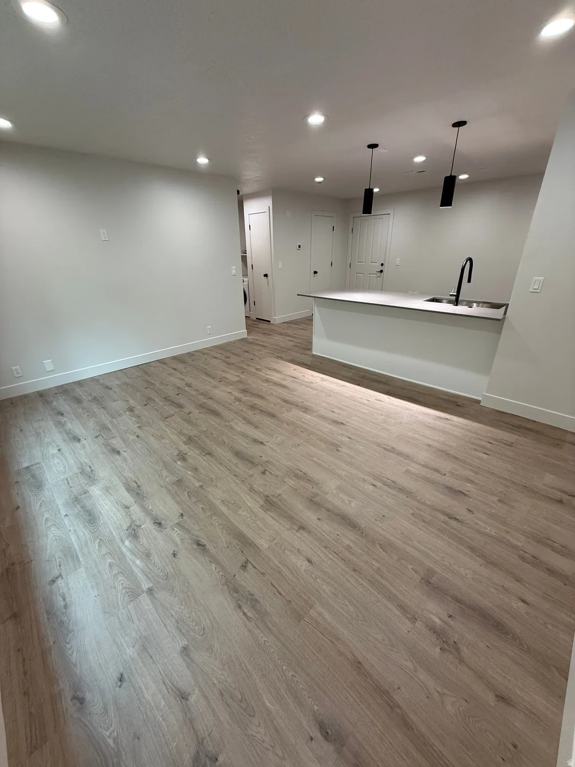 Wood-finish flooring, recessed lighting, and a kitchen island with a single-basin sink and black fixture