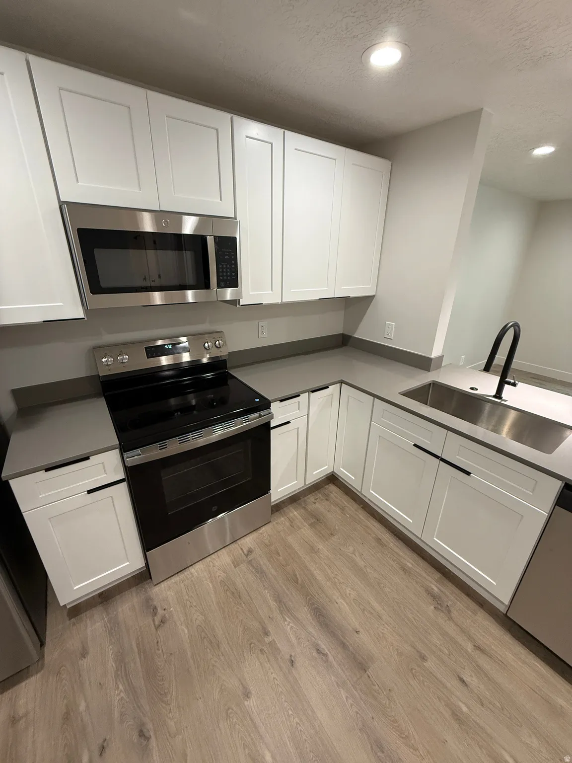 Kitchen featuring white shaker cabinetry, stainless steel appliances, gray countertops, wood-finish flooring, and a stainless steel sink with a matte black faucet