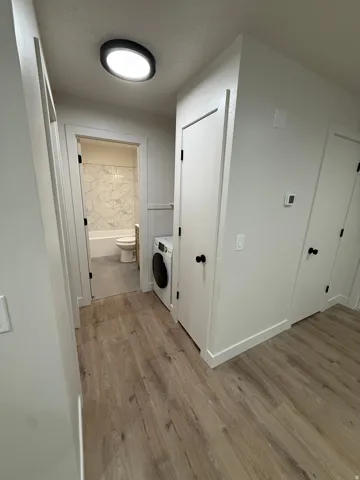 Wood-finish flooring leading to a bathroom with a tiled shower surround