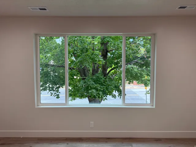 Expansive triple-pane window with white framing, light neutral wall paint, and wood-finish flooring