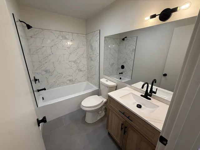 Bathroom featuring a vanity with an integrated sink and wood-finish cabinetry, a large wall-mounted mirror, a bathtub with a shower and white tile surround, and matte black fixtures