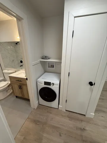 Integrated laundry area with a white front-load washer, wood-finish flooring, and crisp white trim