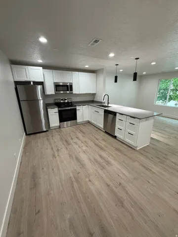 Kitchen featuring stainless steel appliances, white cabinetry, dark countertops, and wood-finish flooring