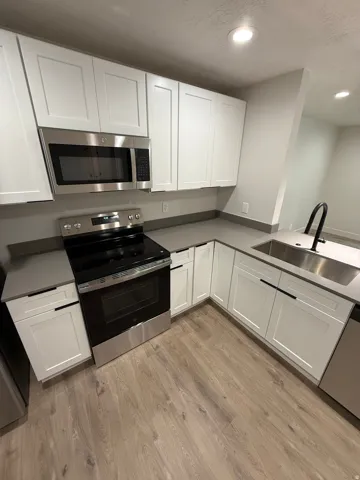 Kitchen featuring white shaker cabinetry, stainless steel appliances, gray countertops, wood-finish flooring, and a stainless steel sink with a matte black faucet