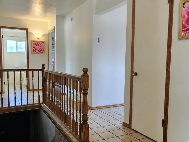 Hallway featuring ceramic tile flooring, wood baluster railing, white walls, and a ceiling access panel