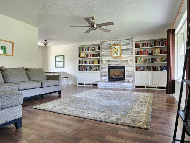 Spacious living area featuring wood-finish flooring, a ceiling fan, and a fireplace with a wood-paneled surround